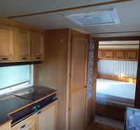 Interior of a motorhome with a kitchenette and bedroom, wooden decor flooring, gardens.
