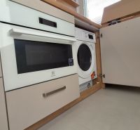 Built-in washing machine and oven in the kitchen unit of a studio apartment with light flooring.