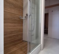 Shower corner with wooden decor in a studio apartment with white tiles.
