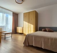 A bright room with a bed, chair, and furniture in a studio apartment, floor with wooden decor.