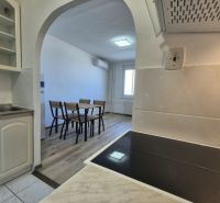 A kitchen with an open passage to the dining table, flooring with a wooden decor.