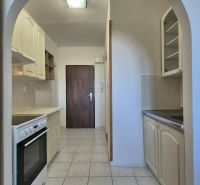 A kitchen in a studio apartment with white cabinets and white tiles on the floor.