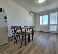 Studio apartment with a refrigerator, wooden decor on the floor, and a dining table with chairs.
