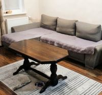 Living room of a three-room apartment with a sofa, table, wood-patterned floor, and carpet.