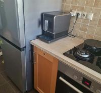 A kitchen in a 3-room apartment with a refrigerator, stove, and coffee maker on a stone countertop.