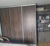 A wardrobe and a bookcase in a 3-room apartment, with a floor featuring a wooden decor.