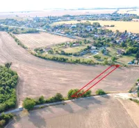 Agricultural and forest lands in Podhájska, surrounding fields and distant buildings.