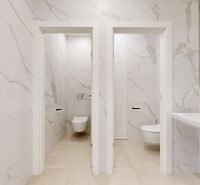 Modern toilets with marble tiles and a sink in the offices.