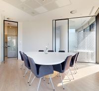 Offices with glass walls, an oval table, gray chairs, and a wood-patterned floor.