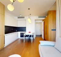 The kitchen of a two-room apartment with white furniture, a wooden decor floor, and a dining table.