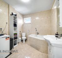A bathroom in a family house with a bathtub, sink, washing machine, and shelving cabinet.