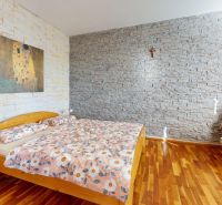A bedroom with stone walls, a bed, and a chair, with a wooden-patterned floor.