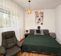 A bedroom in a studio apartment with an armchair, a bed, and a wood-decor floor.
