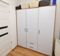 White cabinet with baskets, doors, and floor with wood decor in a studio apartment.
