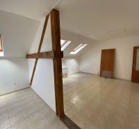 An attic office with wooden beams and slanted windows, floor with wooden decor.