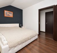 Bright bedroom with a bed and wood-patterned floor in a family house.