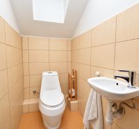 A bathroom in a family house with a toilet and a sink, beige tiles.
