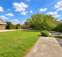 A garden in Mosonmagyaróvár with a lawn, trees, and a concrete path near a family house.