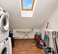 Laundry room in the attic of a family house with a wooden decor floor.