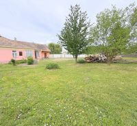 A family house in Dunakiliti with a pink facade surrounded by a spacious garden and trees.