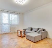 Living room in a two-room apartment with a wooden decor floor and a gray sofa.