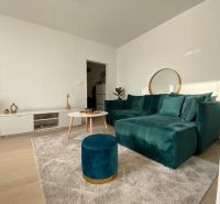 Living room in a three-room apartment with a dark green sofa and a table on a light carpet.