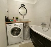 Bathroom of a 3-room apartment with a washing machine, bathtub, sink, and round mirror.