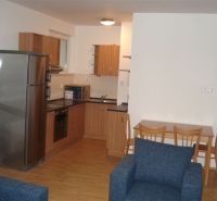 A kitchen in a 3-room apartment with a kitchen unit, dining table, and a floor with a wood decor.