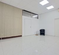 A white room with a ceramic floor, an armchair, a table, and vertical blinds.
