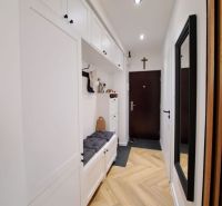 A hallway in a 3-room apartment with a wooden decor floor and white storage cabinets.