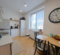 A kitchen in a 3-room apartment with a wooden decor floor, a dining table, and a large clock.