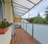 A balcony in a 3-room apartment with a wooden decor floor, flowers, and a view.