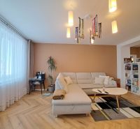 Living room with a white couch, wood-patterned floor, and a bookshelf in a 3-room apartment.