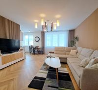 Living room in a 3-room apartment with a sofa, wooden decor, and a dining table in the background.