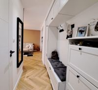 A hallway in a 3-room apartment with white furniture and a wooden decor floor.