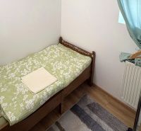 Single bed, clothing rack, green curtains, wood-patterned floor.