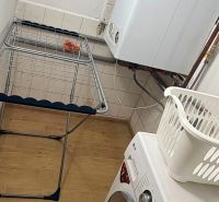 Laundry room in a family house with a washing machine, drying rack, and wooden decor flooring.