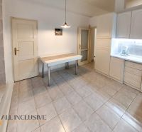 A kitchen in a 2-room apartment with white cabinets, a table, and tiles.