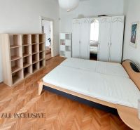 Bedroom in a 2-room apartment with wood-patterned flooring, a bed, a wardrobe, and shelves.