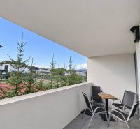 A balcony of a 2-room apartment with seating, a view of greenery, and modern tiles.