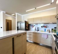 The kitchen of a three-room apartment with a wooden decor floor and light furniture.