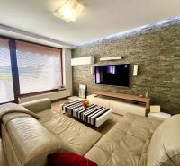 Living room in a 3-room apartment with a leather sofa, stone wall, and floor with a wooden decor.