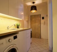 A kitchenette in a studio apartment with wooden floor decor and white cabinets.