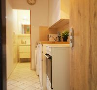 A kitchenette in a studio apartment with white cabinets and appliances, tiled flooring.
