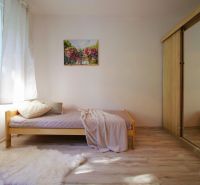 A studio apartment with a simple bed, a wardrobe, and a floor with a wooden decor.