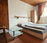 Bedroom of the vacation apartment with a double bed, armchairs, and a window, floor with wooden decor.