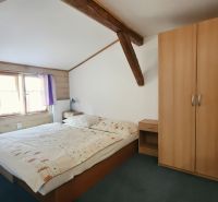 Bedroom in a holiday apartment with wooden beams, a wardrobe, and a bed next to the window.