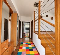 Interior of a family house with a staircase made of wood decor and a colorful carpet.