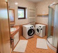 A bathroom in a family house with a washing machine, dryer, and shower enclosure.