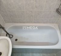 A bathroom with a bathtub and a sink in a two-room apartment, tiled with light tiles.